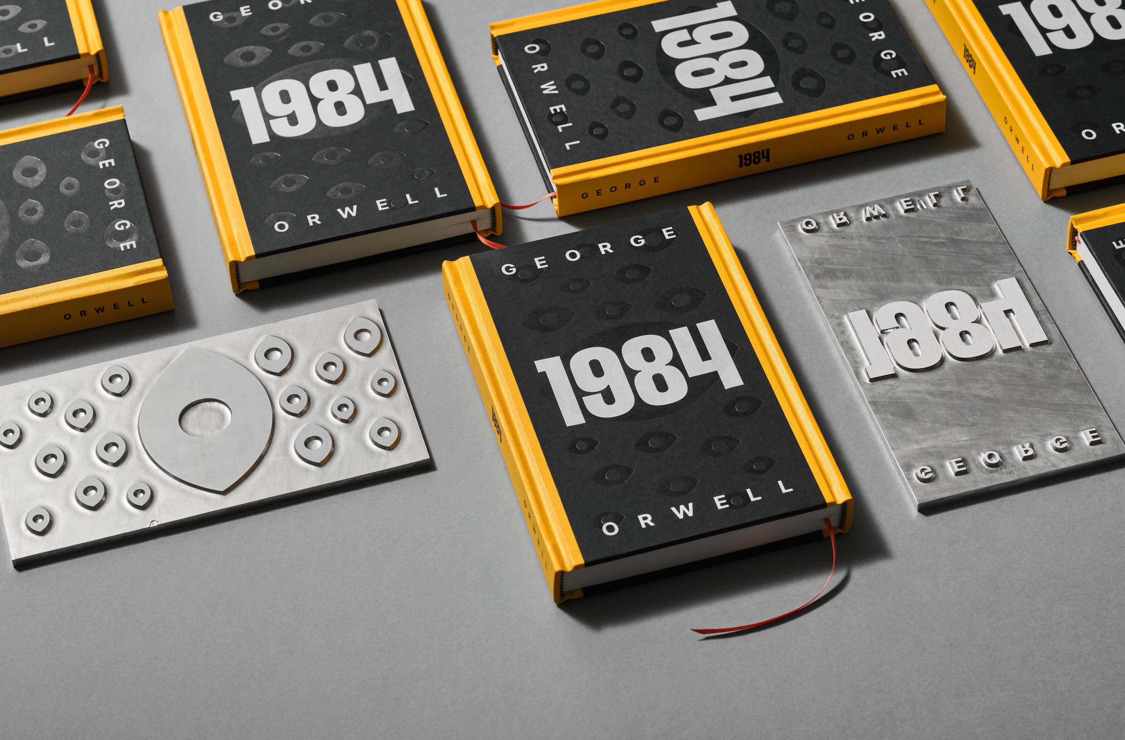 Multiple copies of the book 1984 by George Orwell with black covers and yellow spines, alongside metal printing plates for the cover design.