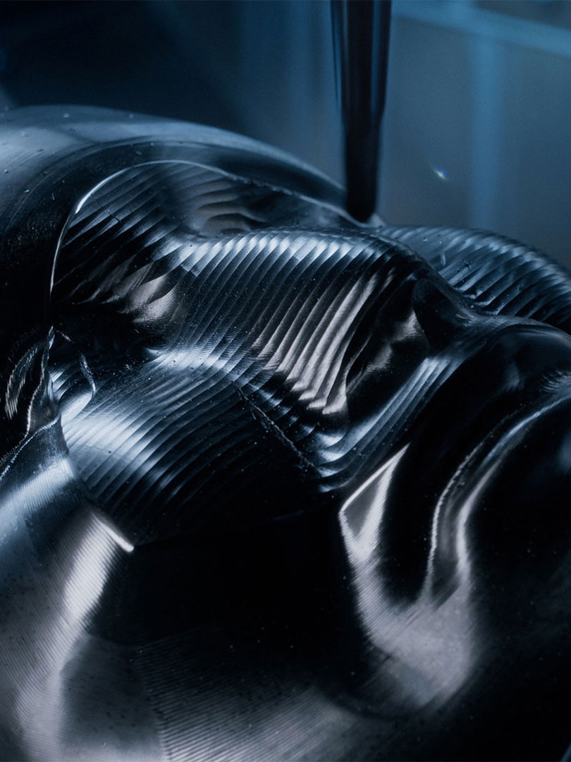 Close-up of a black, ribbed surface resembling a sculpted human face with light reflections highlighting its contours.