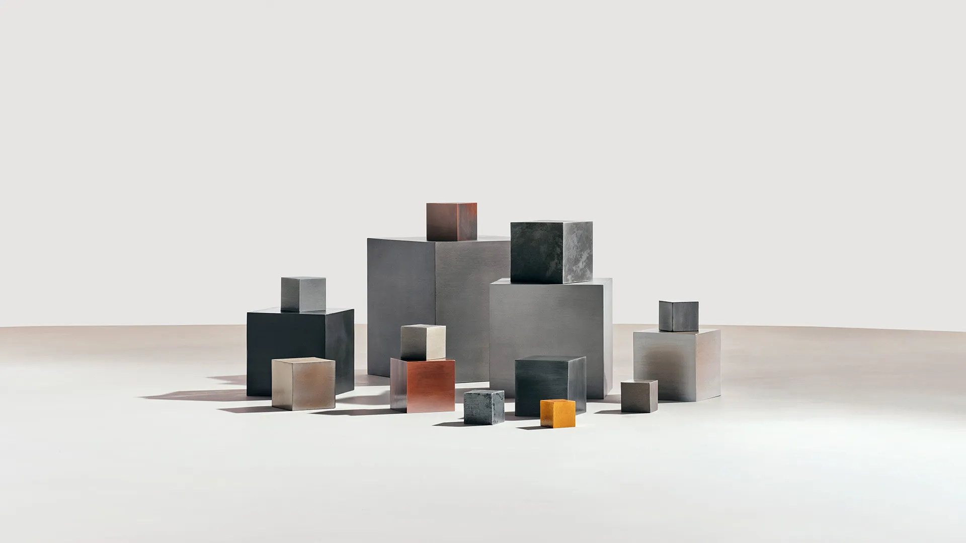 Various metal cubes of different sizes and finishes arranged on a white surface with shadows.