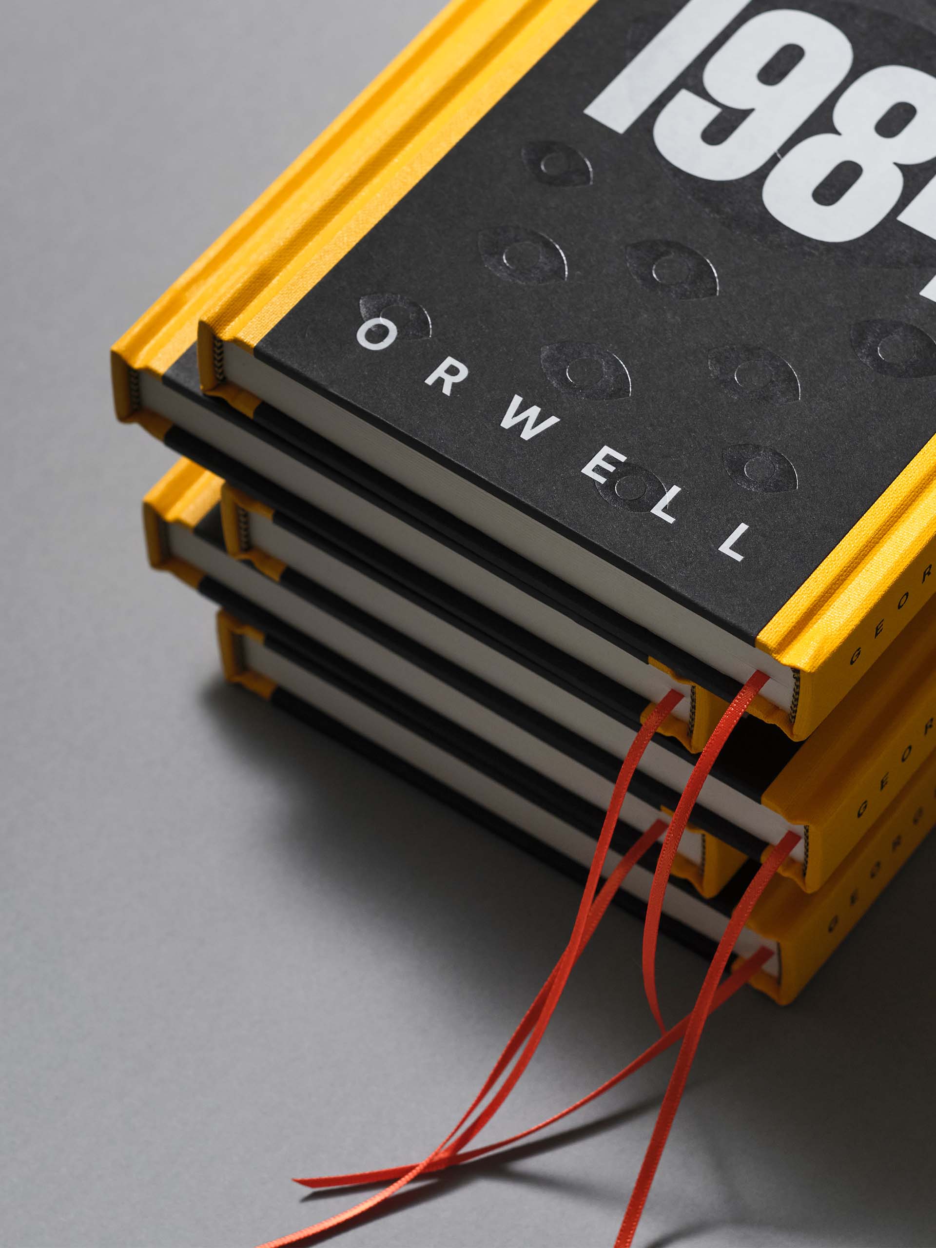 Stack of four yellow and black hardcover books titled '1984' by Orwell, with red ribbon bookmarks.