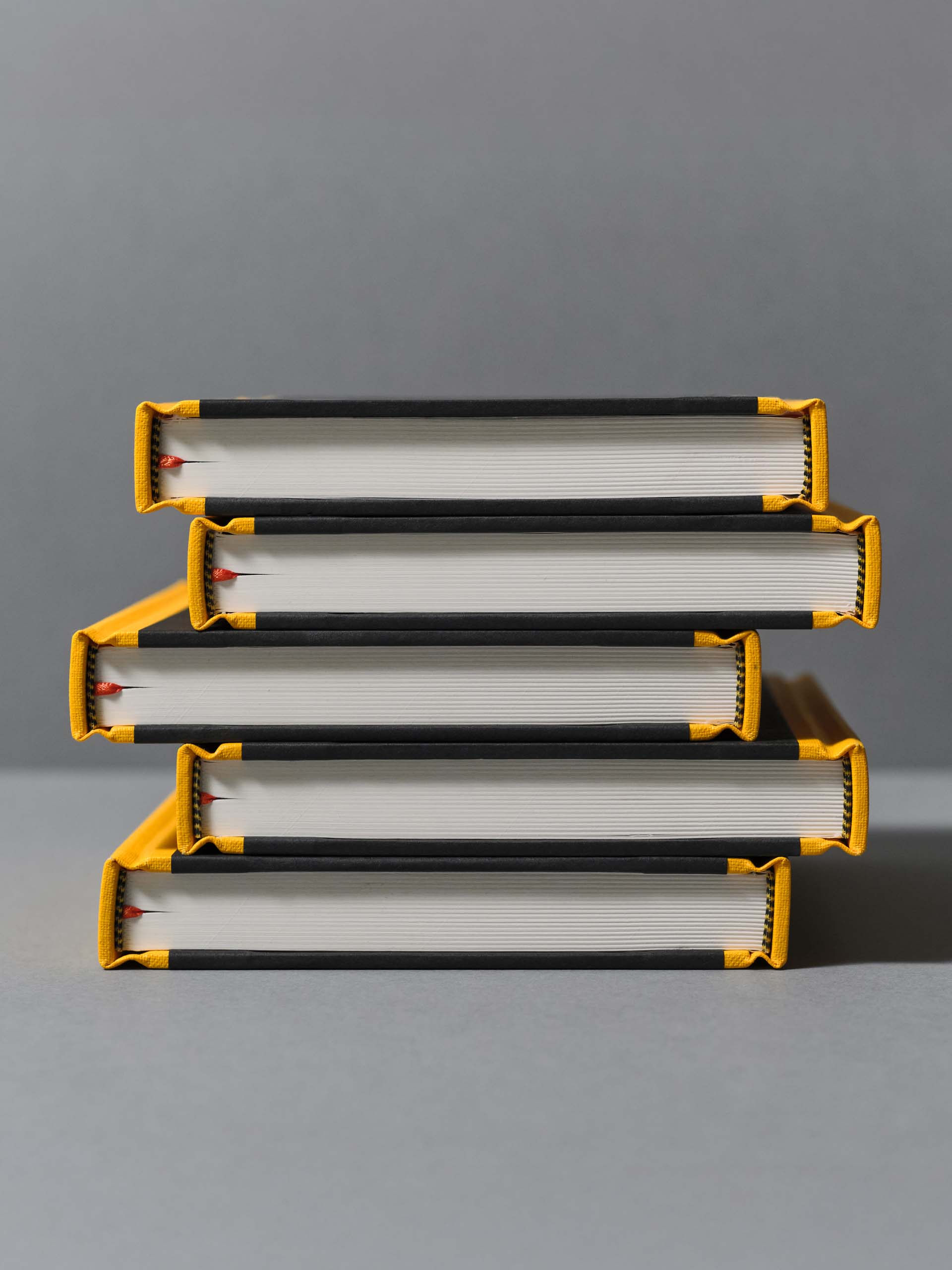 Stack of five hardcover books with black and yellow spines on a gray surface against a gray background.
