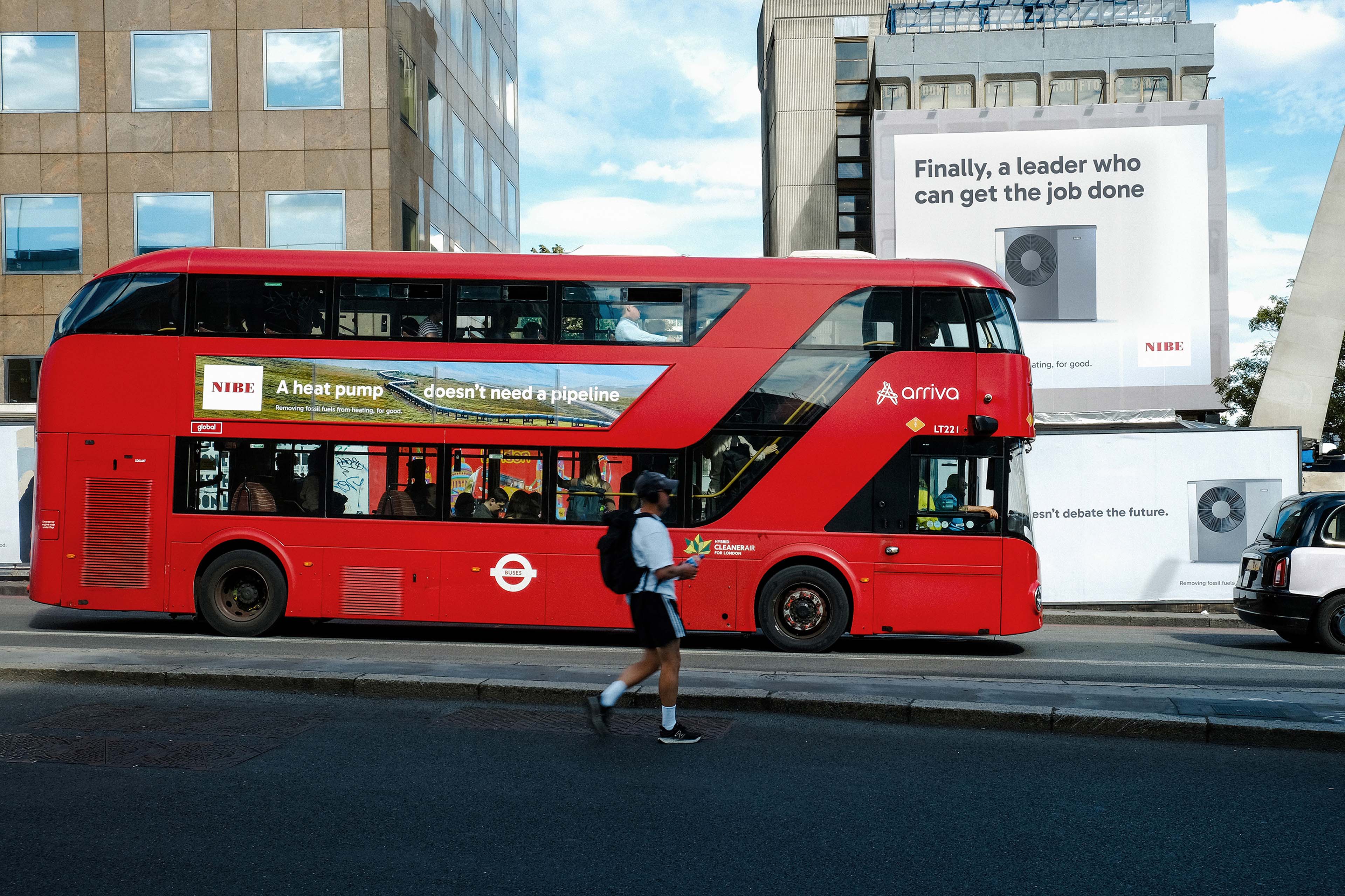 NIBE ad on a red double decker bus that reads "A heat pump doesn't need a pipeline", two NIBE bilboards in the background that read "Finally a leader who can get the job done"