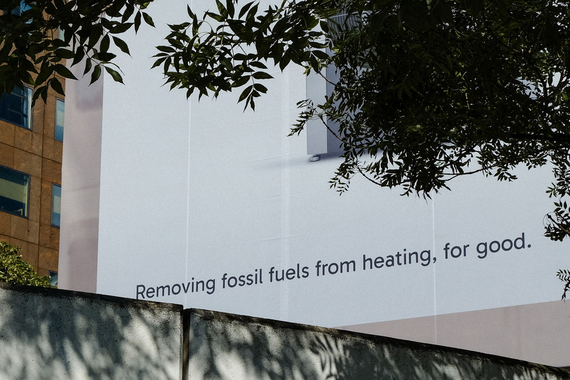 Billboard with text: Removing fossil fuels from heating, for good, partially obscured by tree and wall shadows.